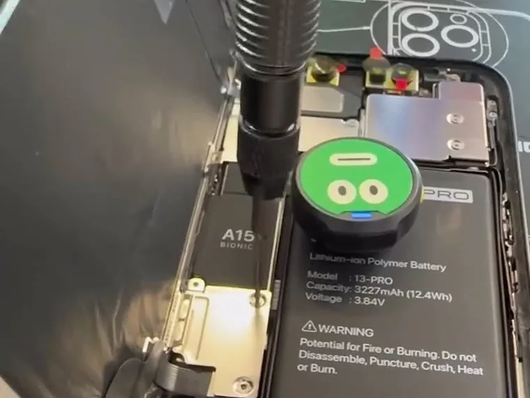An opened iPhone 13 Pro on a schematic mat, A15 board shield and battery visible