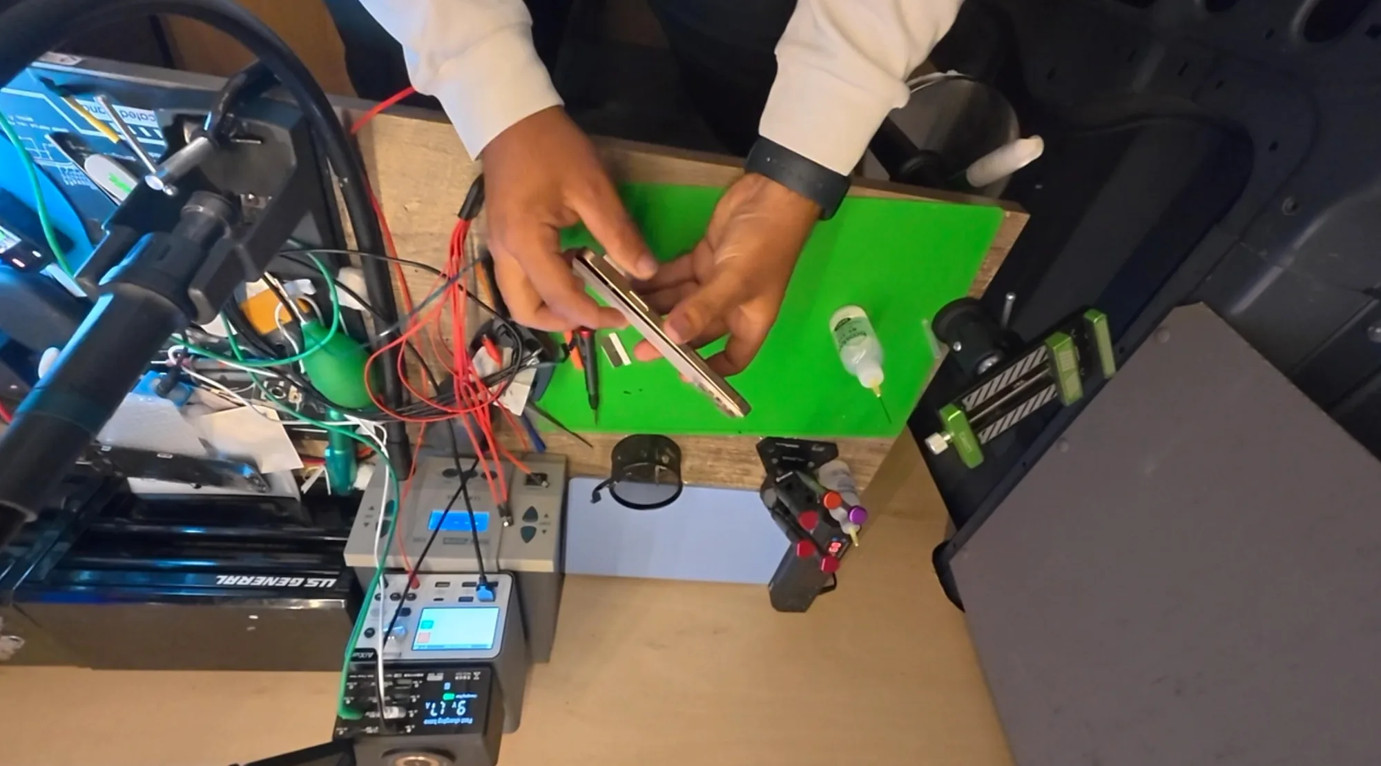 A technician probing an opened iPhone on a green anti-static mat with a bench power supply